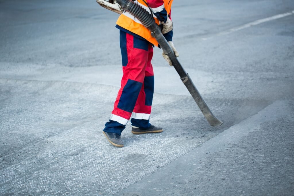 Worker with leaf-blower, cleaning out the dust for better asphalt adhesion